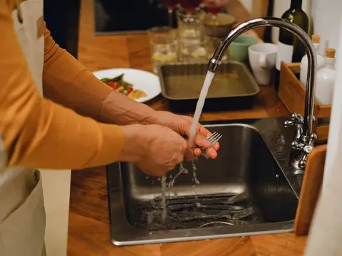 A fork rinsed under running water at a kitchen sink
