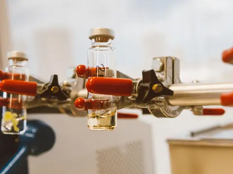 Glass sample vials held in a clamp with red handles