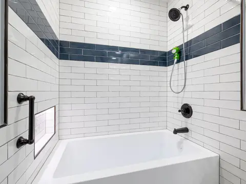 A white tiled bathtub alcove with black fixtures