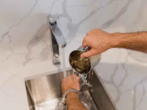 A metal cup filled at a tap over a steel sink