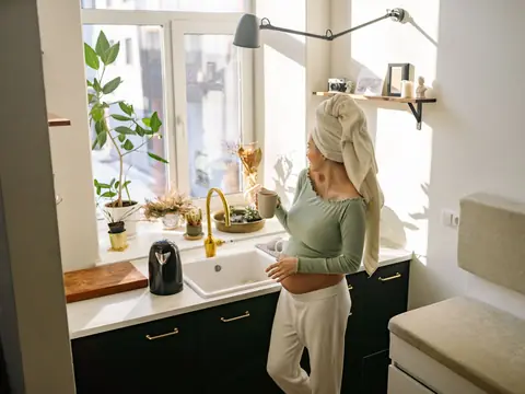 A bright kitchen with a gold faucet below a window full of plants