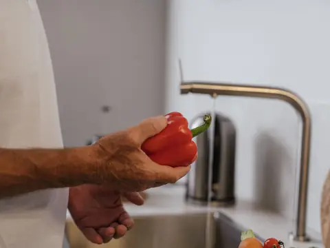 A red pepper rinsed under a brushed steel kitchen faucet