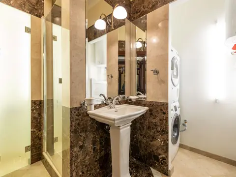 A small bathroom with a pedestal sink, a stacked washer and a wall water heater