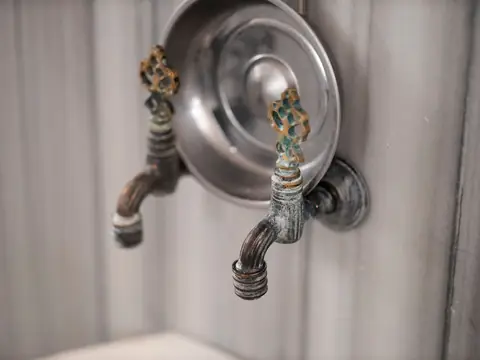 Two old brass taps on a gray wall