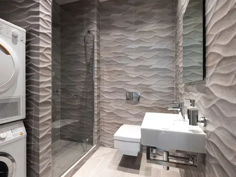 A gray tiled bathroom with a stacked washer and dryer and a glass shower