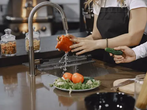 Water splashing from a pull-down kitchen faucet as a pepper is rinsed