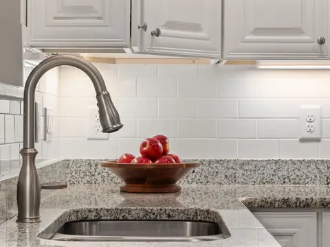 A pull-down faucet over an undermount sink in a granite counter, a bowl of red apples beside it