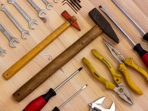 Wrenches, pliers, screwdrivers and hammers laid out on a wooden bench