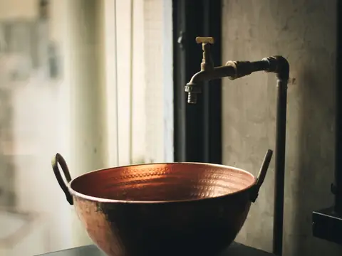 A copper bowl under an old brass tap