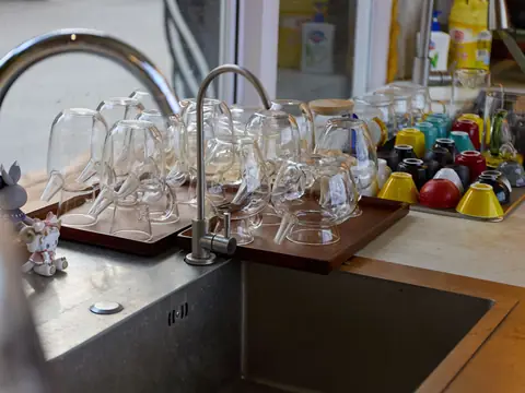 Glasses and cups drying beside a kitchen sink in bright light